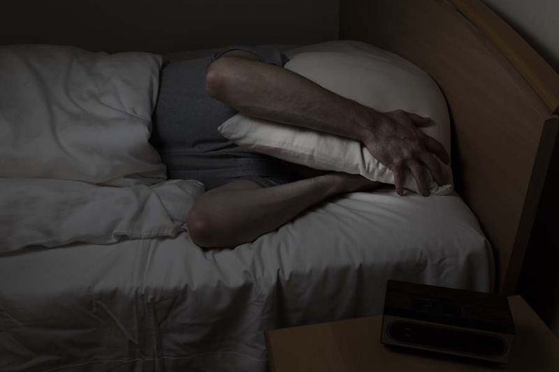 Blog Title: Why Is My Air Conditioner Making Noise? Photo: Mature man, with pillow covering entire face, cannot sleep at night