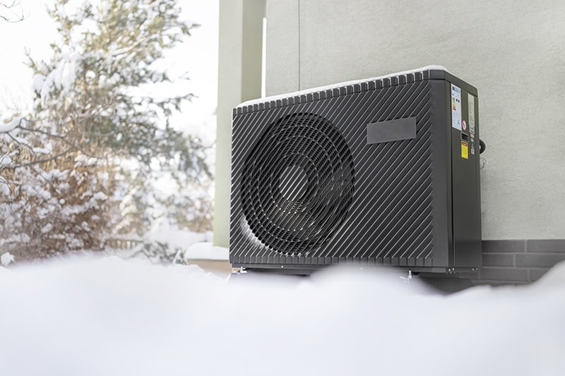 A modern air-source heat pump unit installed against the exterior wall of a building.
