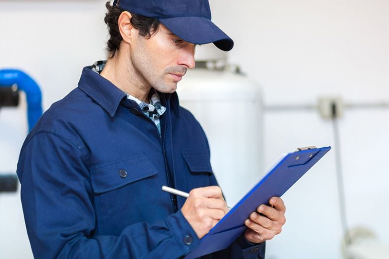 A technician studies a clipboard. Schedule Your Annual Furnace Inspection Now.